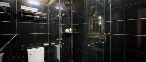 Une salle de bain comprenant des toilettes, une douche fermée par une paroi de verre et une étagère avec des articles de toilette.