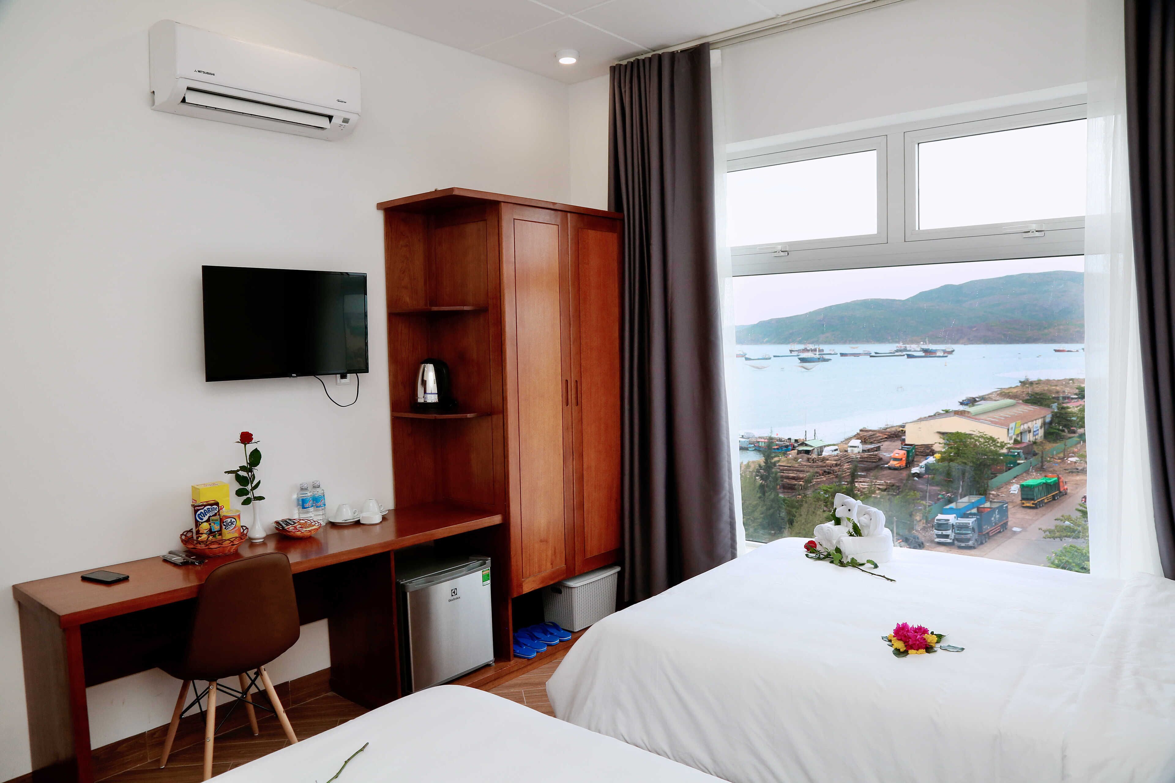 A hotel room with a bed, a desk, a television, a wardrobe, and a window with a view of boats and a dock.