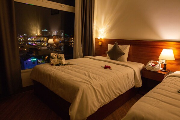 A hotel room with a large bed, a smaller bed, a nightstand with a lamp, and a view of a cityscape at night. - Thanh Van Hotel (Quy Nhon)