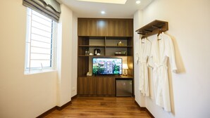Une chambre d’hôtel avec un plancher en bois, une télévision, un mini-réfrigérateur et un porte-peignoirs blanc.