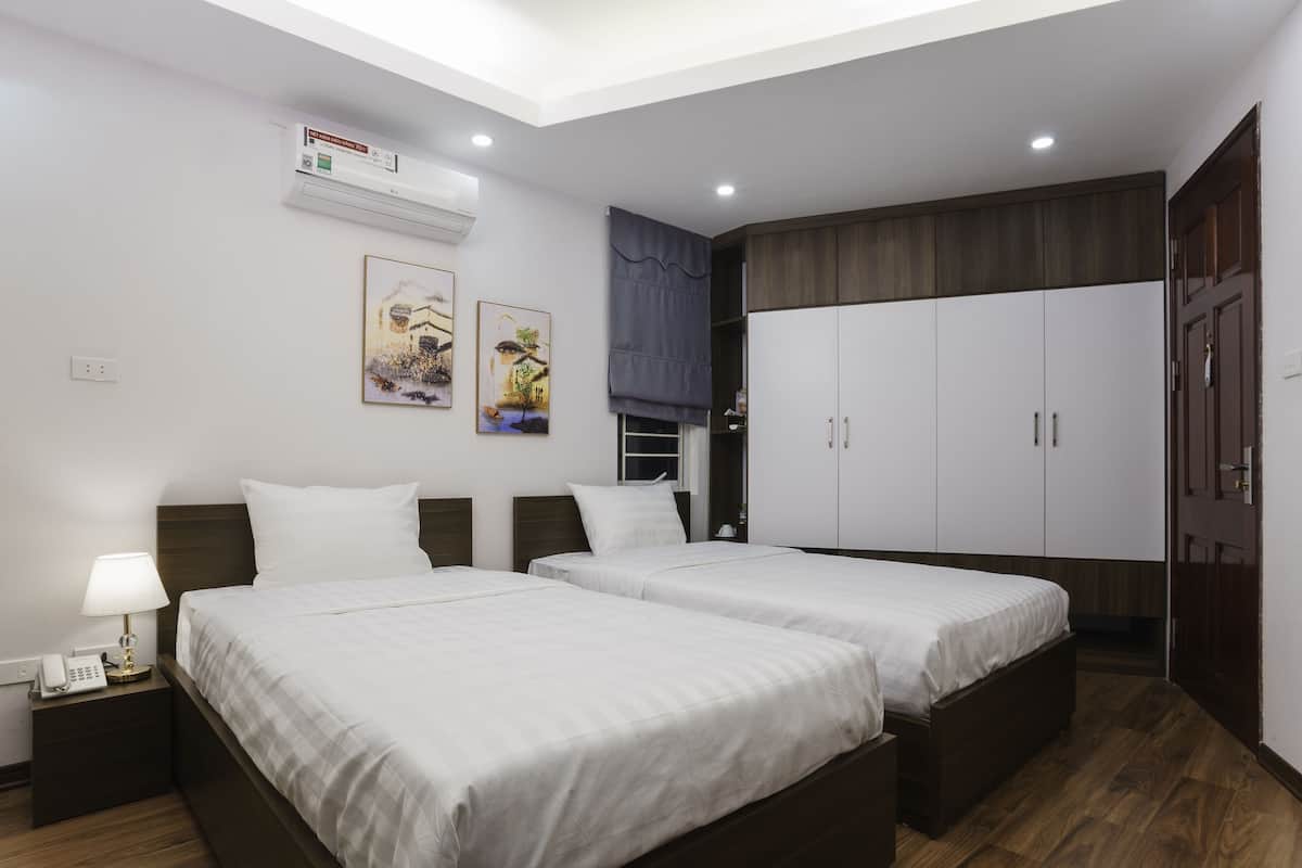 Habitación de hotel con dos camas, un armario, una mesita de noche con lámpara y aire acondicionado instalado en la pared.