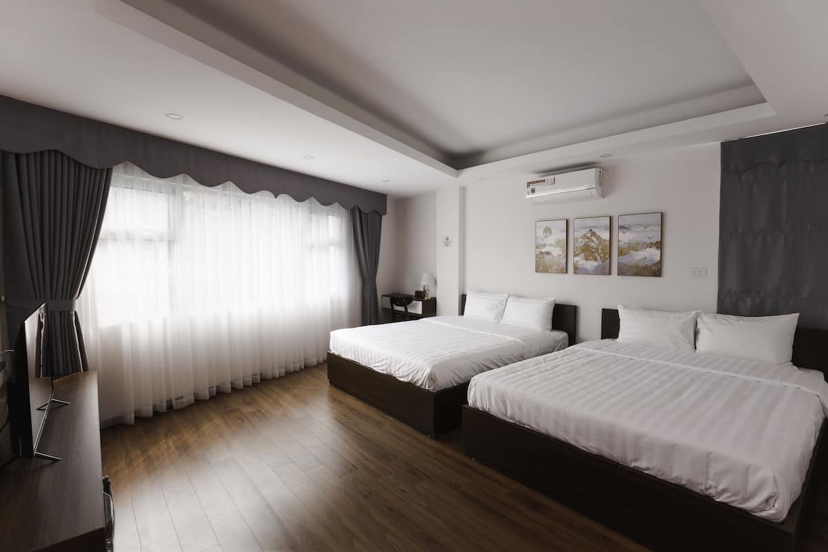 Una habitación de hotel moderna con dos camas, un escritorio y un amplio ventanal con cortinas.