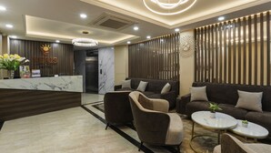 Un hall d’accueil d’hôtel avec un comptoir en marbre, des canapés sombres et un lustre moderne.