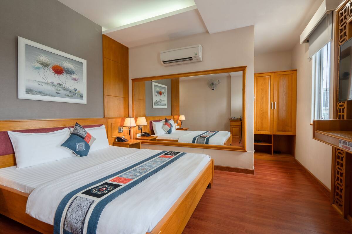 Een hotelkamer met twee bedden, een grote spiegel, houten meubels en een airconditioning.