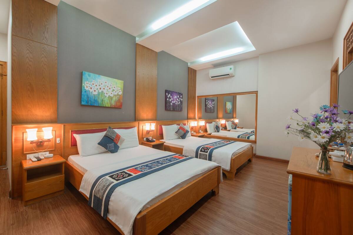 Een hotelkamer met twee bedden, houten hoofdeinden, nachtkastjes met lampen, een spiegel en kunstwerken aan de muur.