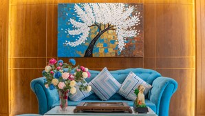 Un canapé bleu orné de coussins à motifs, un vase de fleurs et un plateau posé sur une table blanche, le tout adossé à un mur en bois.