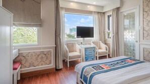 Une chambre d’hôtel avec un grand lit, un bureau avec une chaise, une télévision et une fenêtre avec des rideaux.