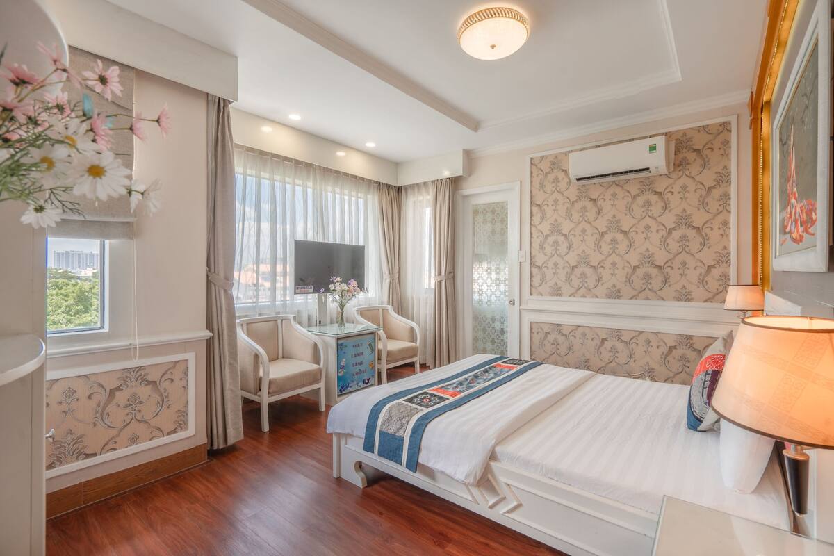 Een hotelkamer met een bed, nachtkastje, stoel, televisie en een raam met gordijnen.
