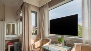 Une pièce dotée d’une grande fenêtre, d’un téléviseur, d’un bureau, d’une chaise et d’une petite table sur laquelle est posé un objet décoratif.