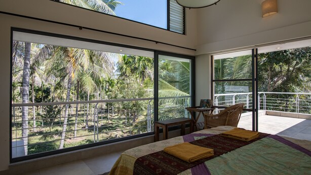 Un dormitorio con ventanas amplias, una cama, un escritorio y una silla.