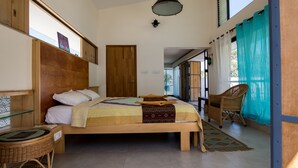 Un dormitorio con cama de madera, repisa de vidrio, silla de mimbre y vistas al exterior.
