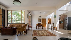 Amplia sala de estar con un ventanal, una mesa de comedor y una cocina al fondo.