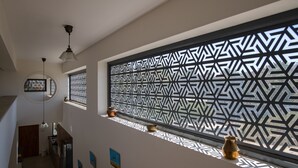 Un pasillo estrecho con un separador decorativo, una lámpara de techo y una ventana con persianas caladas.