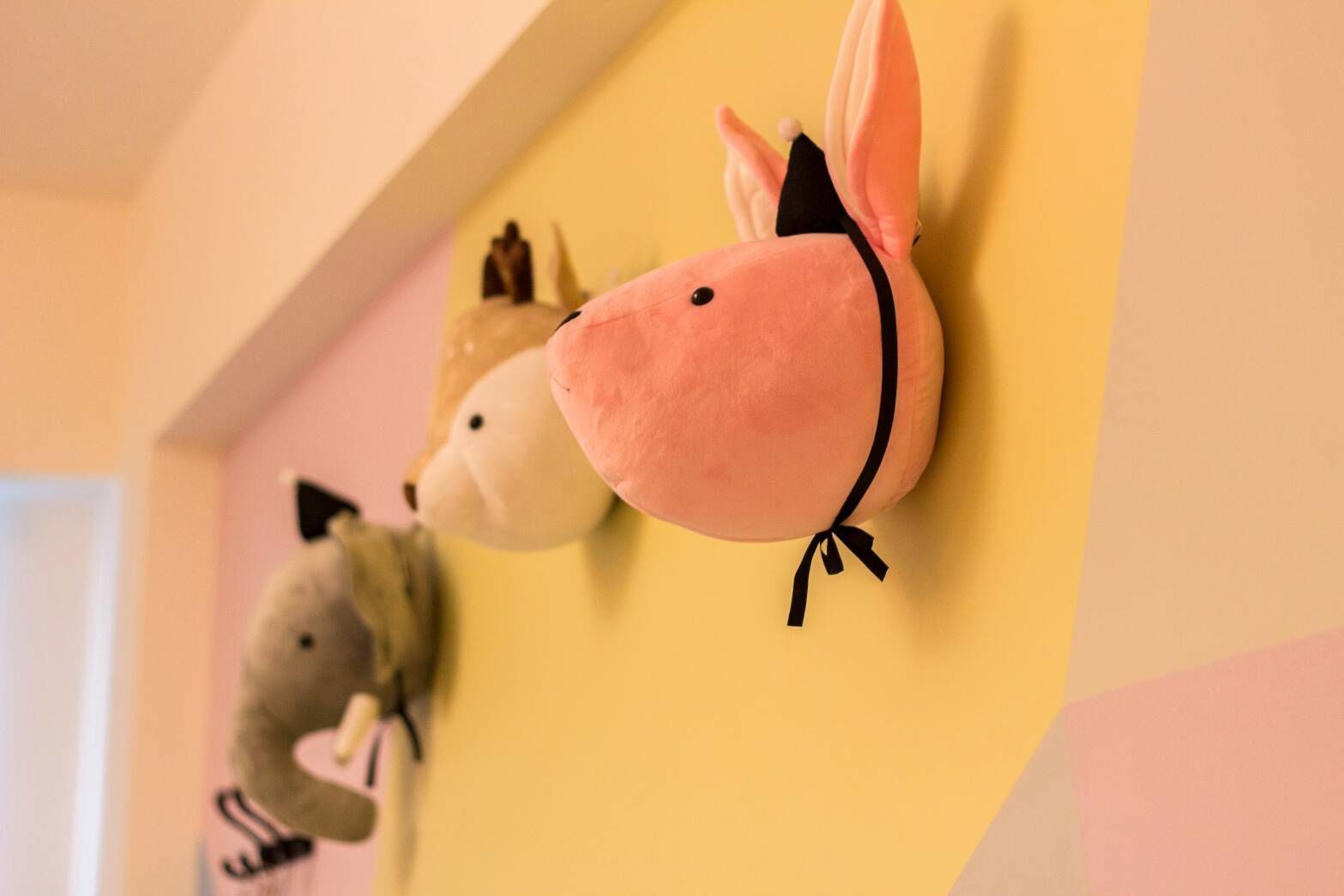 Plush animal wall decorations in a room with a yellow wall and a white door.