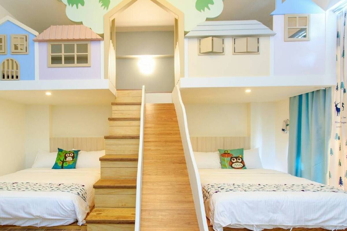 A hotel room with two beds, a wooden staircase, and a ceiling with house-shaped decorations.
