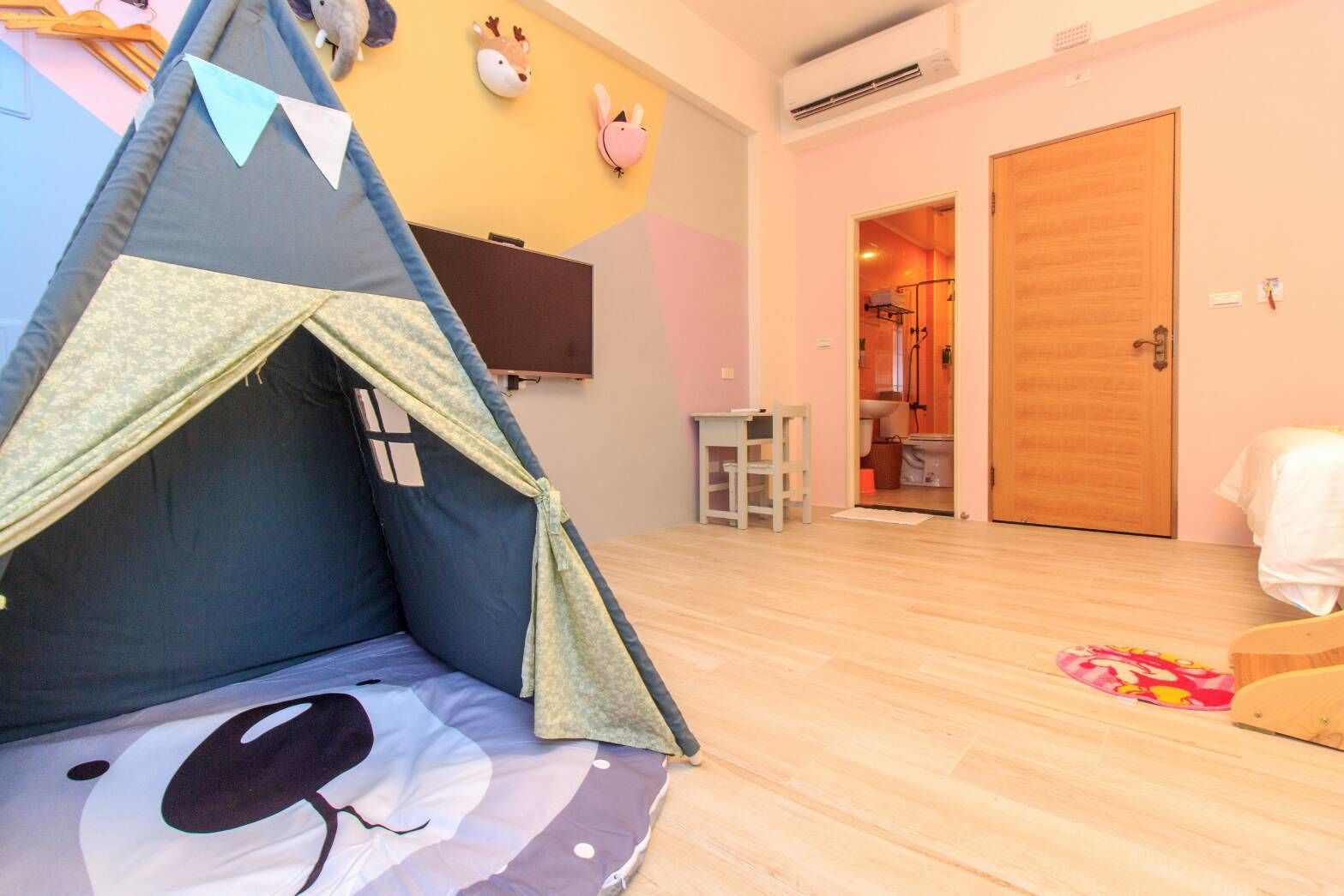 Una habitación con una cama tipo tienda de campaña, una puerta de madera, una mesita y un televisor en la pared.