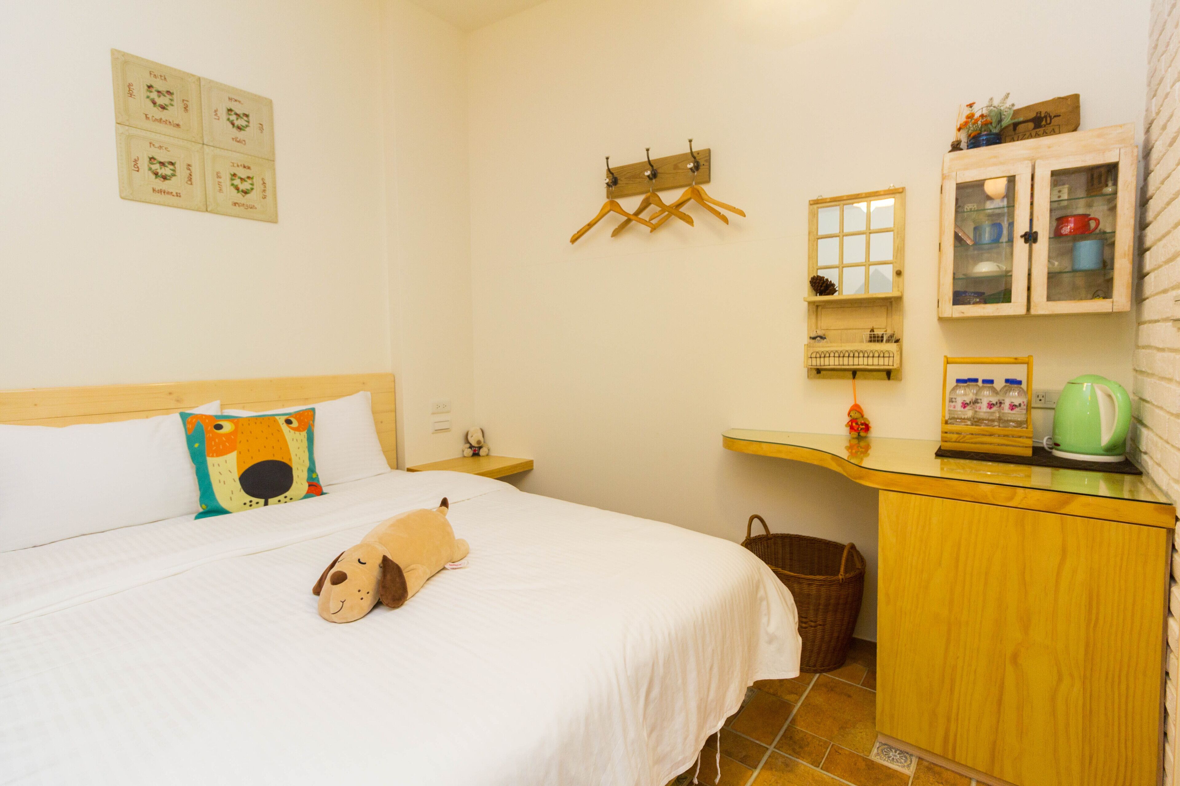 A neatly arranged bedroom with a bed, a wooden dresser, a small table, and a wall-mounted drying rack.
