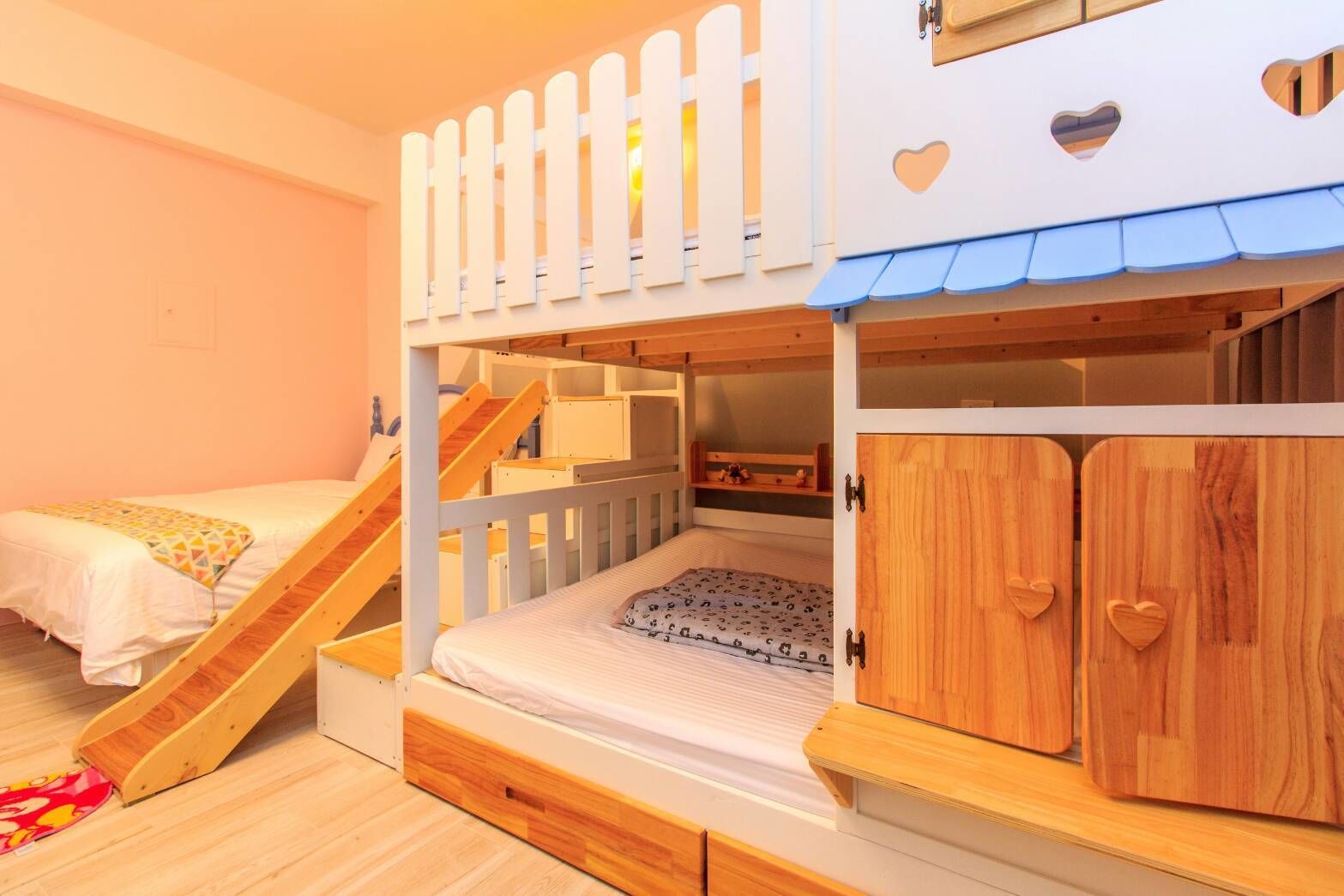 A bunk bed room with a wooden ladder, a small desk, and a wardrobe with heart-shaped handles.
