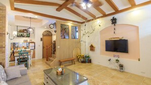 A spacious living area with a glass coffee table, a sofa, a kitchen area with a tiled backsplash, and a staircase leading to another level. - BJ Classic Town (Wujie)