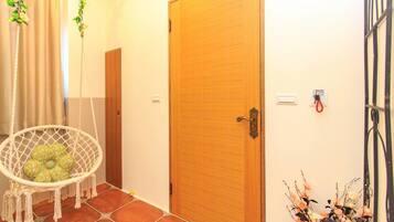 A hallway with a wooden door, a white macrame chair, and a wall-mounted light switch.