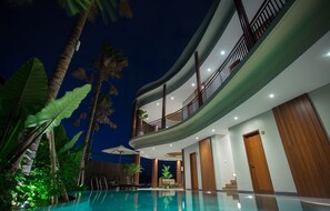 A modern hotel with a curved balcony, a swimming pool, and tropical plants. - Curve House Umalas (Kerobokan)