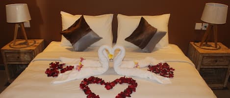 A neatly made bed with a heart-shaped arrangement of rose petals and two swan-shaped pillows.