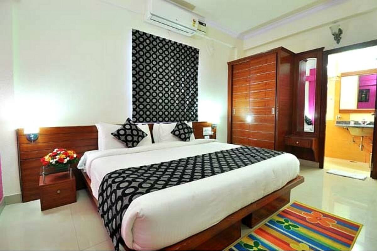 A bedroom with a bed, wooden wardrobe, and a small bedside table with a vase of flowers.