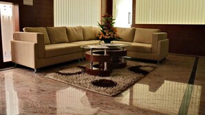 Una sala moderna con un sofá seccional color beige, una mesa de centro de vidrio y un jarrón decorativo con flores.
