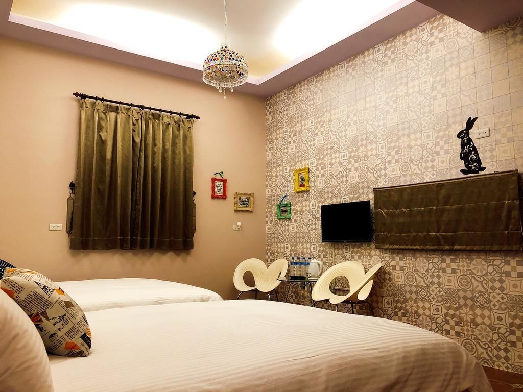 A hotel room with two beds, a chandelier, patterned wallpaper, a television, and a shelf with a statue.