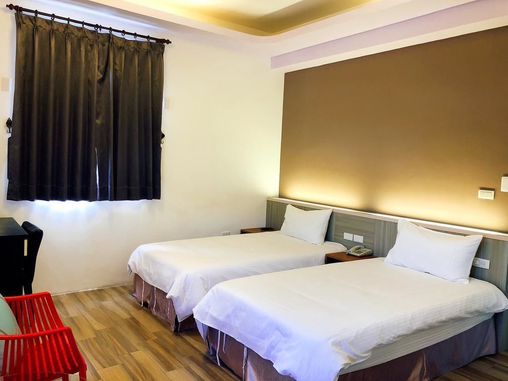A hotel room with two single beds, a desk, and a chair.