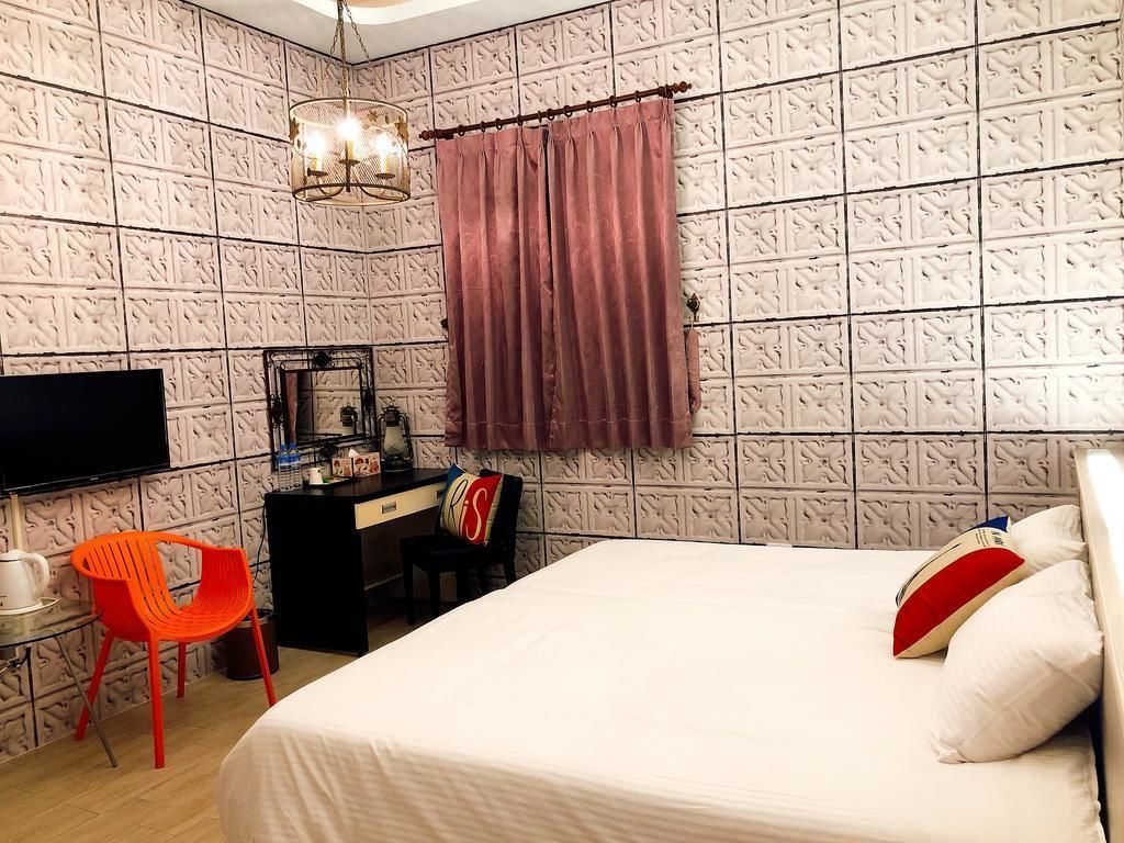 A bedroom with a bed, a desk, a chair, a television, and a chandelier.