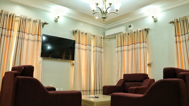 A living room with two brown sofas, a flat-screen TV, and beige curtains. - Bayse One Premium (Ibadan)