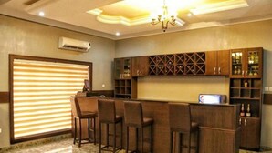 A bar area with a counter and stools, a chandelier, and wooden cabinets with glass doors. - Bayse One Premium (Ibadan)