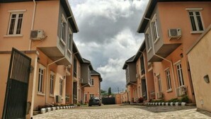 A row of two-story buildings with a paved driveway and a car parked in front. - Bayse One Premium (Ibadan)