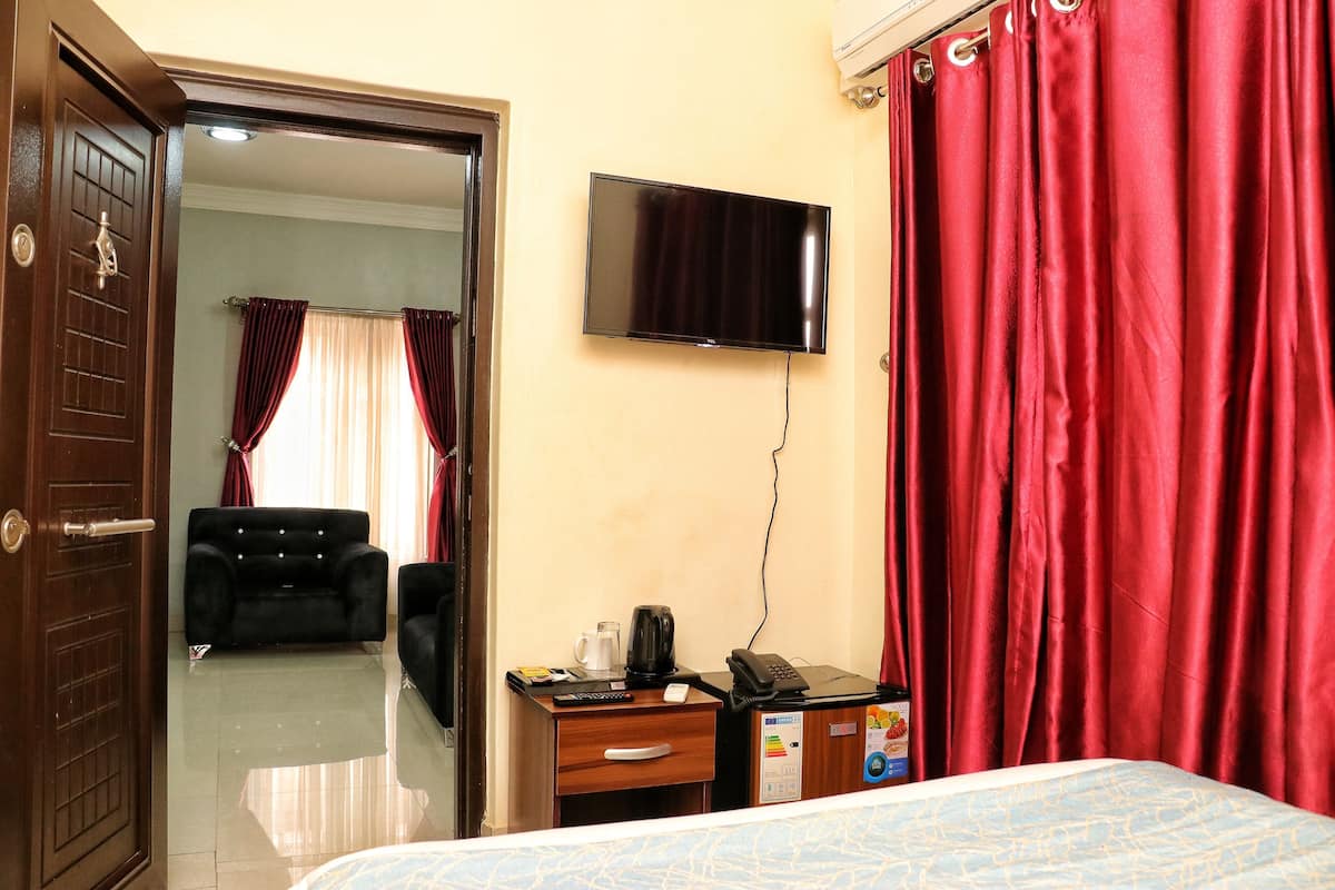 A hotel room with a bed, a desk with a telephone and a coffee maker, a television on the wall, and a door leading to another room.