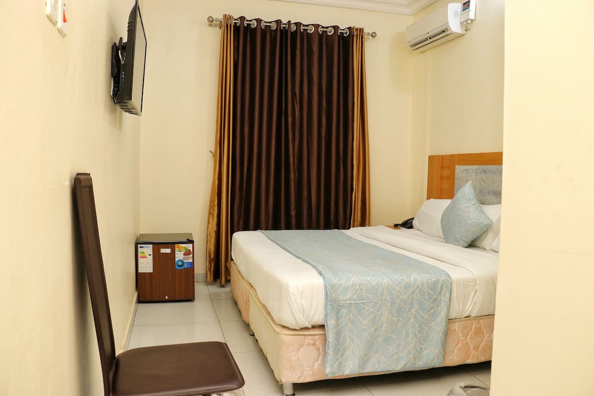 A hotel room with a bed, a chair, a small table, and a curtain.