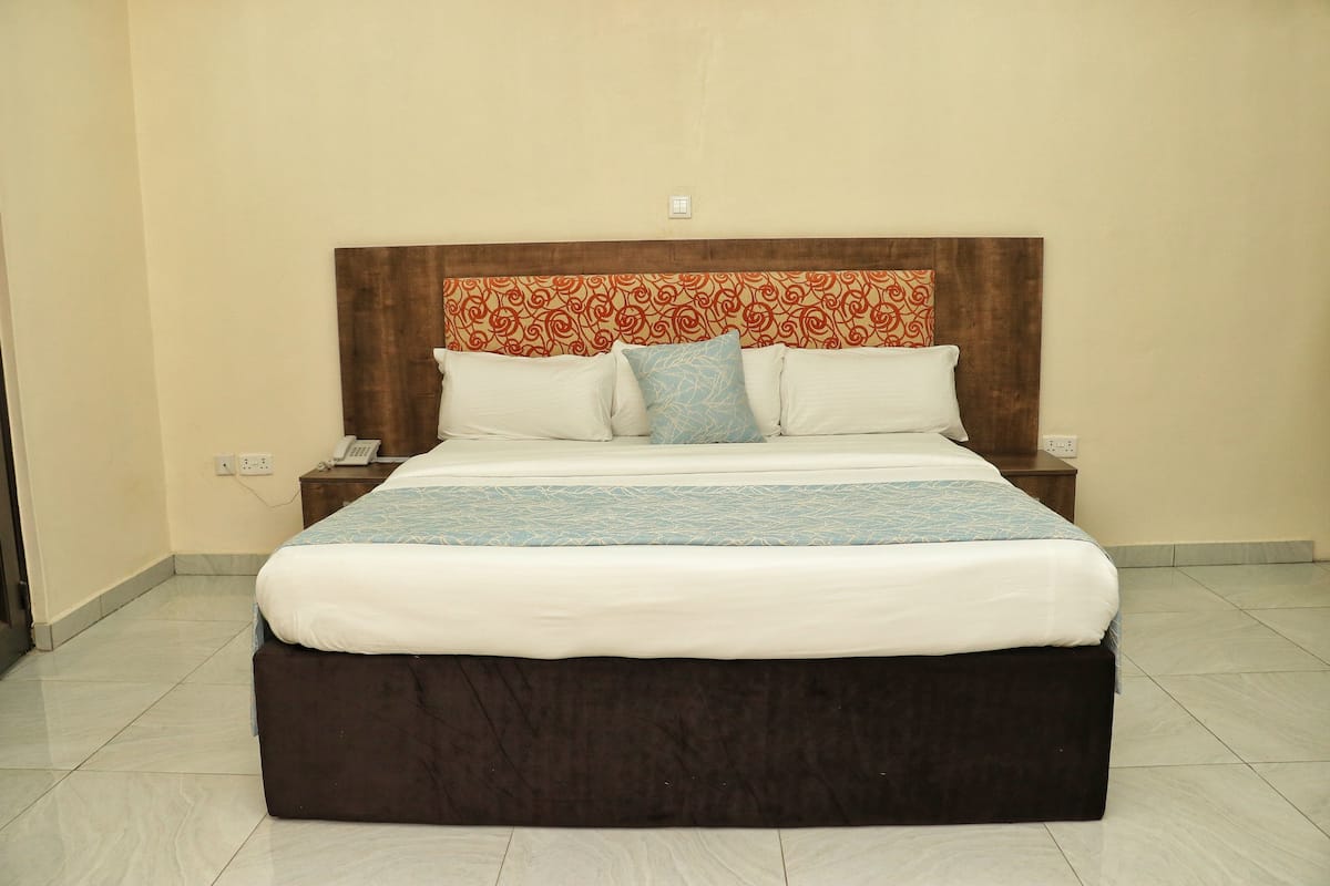 A neatly made bed with a brown headboard, white bedding, and a blue accent pillow.