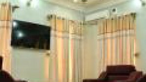 A living room with a flat-screen TV mounted on the wall, two dark-colored sofas, and a chandelier. - Bayse One Premium (Ibadan)