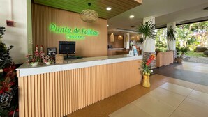A reception desk at Pluncla de Fabian Resort with a wooden panel design, a neon sign, and a view of the outdoor area with plants and a covered seating area. - Punta de Fabian powered by Cocotel (Baras)
