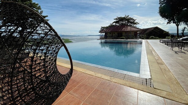 A pool area with a wicker chair, a building with a red roof, and a view of the sea. - Punta de Fabian powered by Cocotel (Baras)