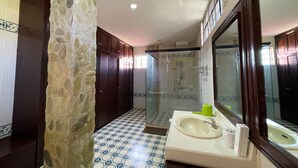 A bathroom with a stone column, a sink with a mirror, and a shower area. - Punta de Fabian powered by Cocotel (Baras)