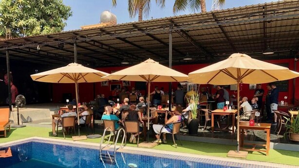 An outdoor pool area with multiple tables and chairs, umbrellas, and a covered seating area. - Downtown Siem Reap Villa (Siem Reap)