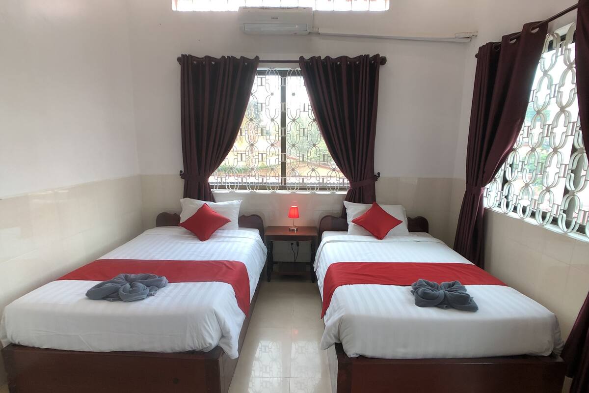 Een kamer met twee bedden, elk met een rode en witte dekbedovertrek, en een kleine tafel ertussen.