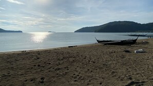 Uma praia com barcos, céu claro e uma montanha ao longe.