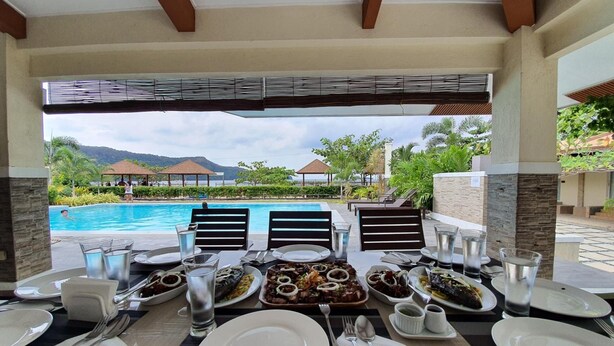 Mesa de jantar posta para uma refeição, com vista para uma piscina e montanhas ao fundo.