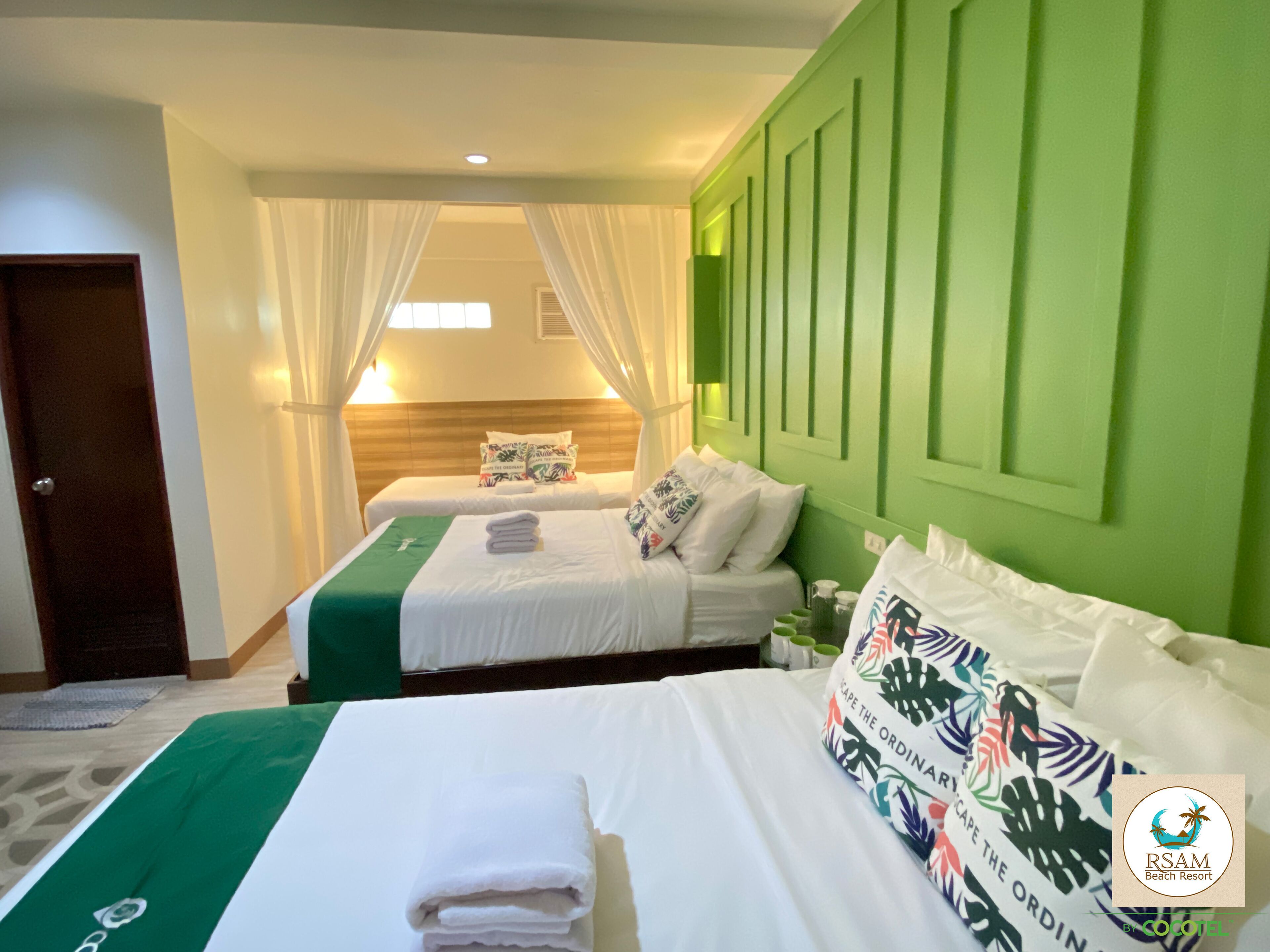 A hotel room with two beds, a green accent wall, and a window with curtains.