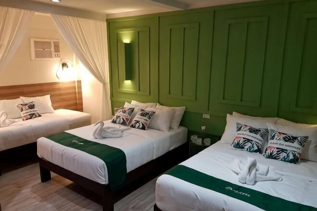 Ein Hotelzimmer mit zwei Betten, jeweils mit weißer Bettwäsche und grünen Kissen, einer grünen Akzentwand und einem Nachttisch mit einer Lampe.
