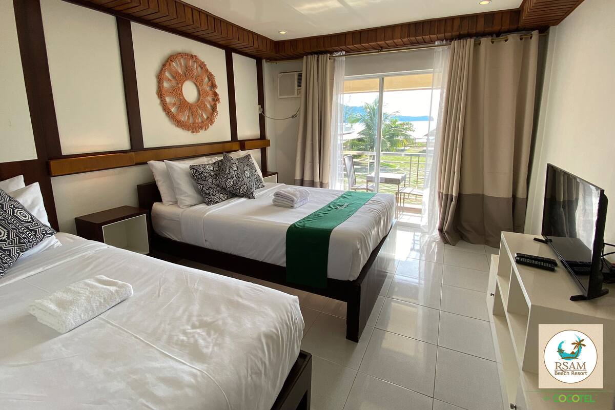 Ein Hotelzimmer mit zwei Betten, einem Fernseher und einem Balkon mit Blick auf den Strand.