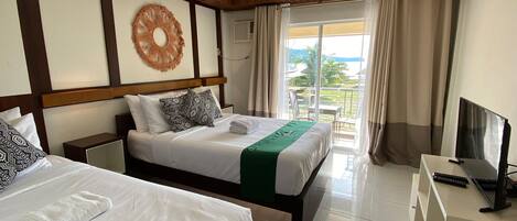 Una habitación de hotel con dos camas, televisión y balcón con vista a la playa.