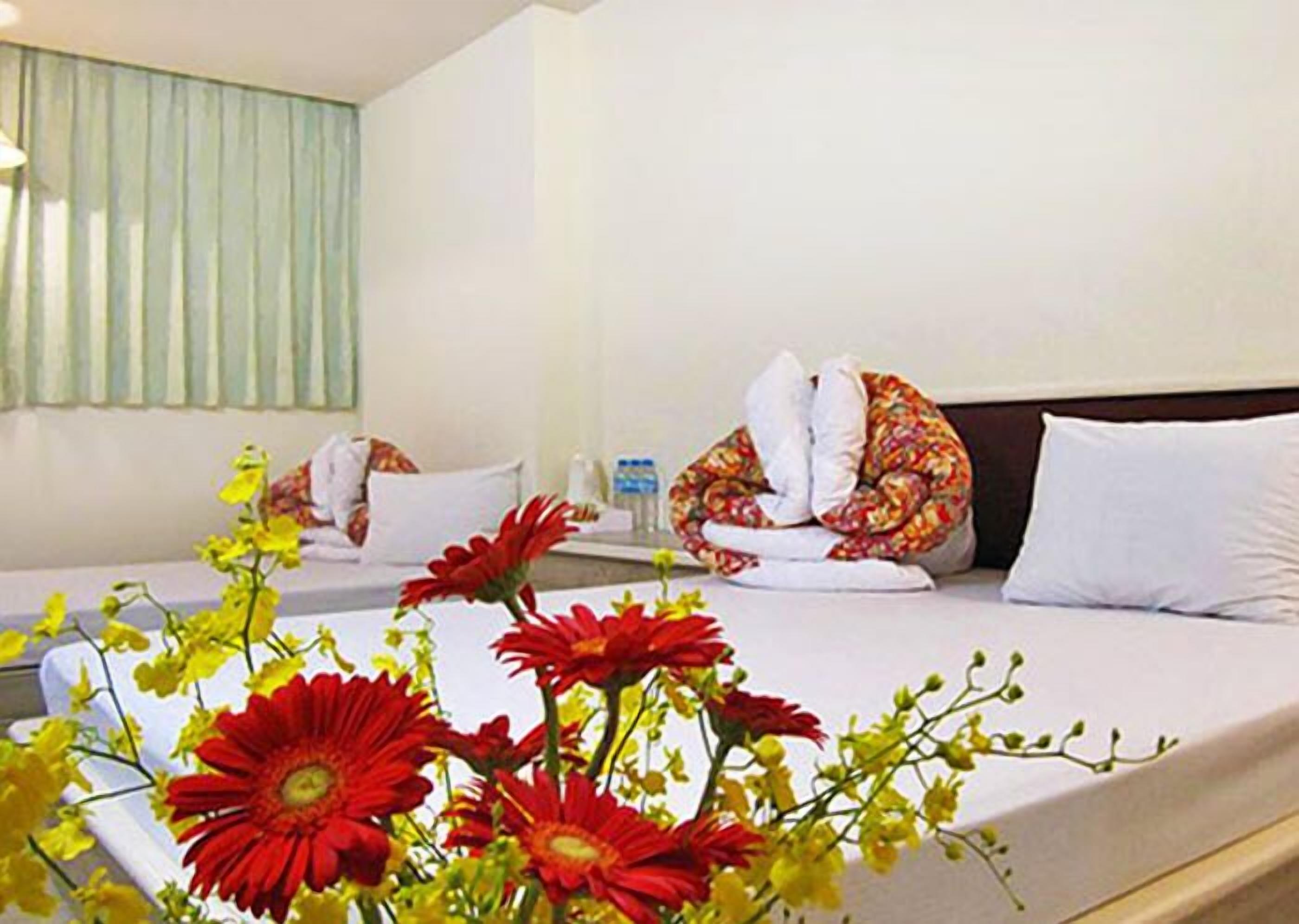 A hotel room with a bed, pillows, a bedside table, and a vase of flowers.